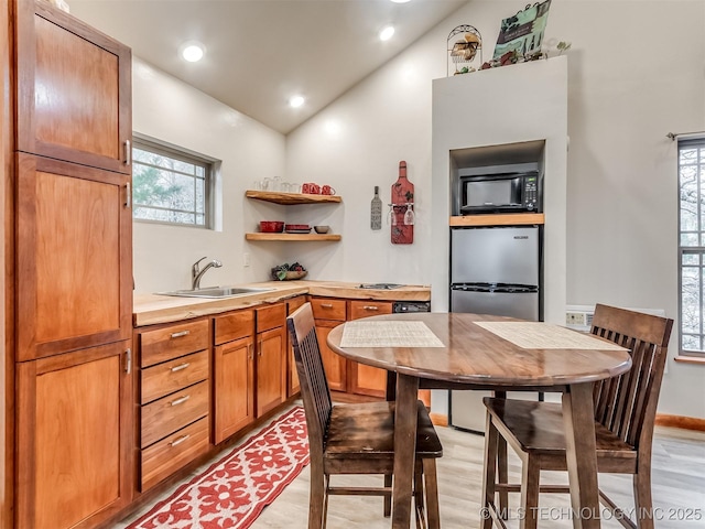 kitchen with stainless steel fridge, light wood-type flooring, lofted ceiling, and sink