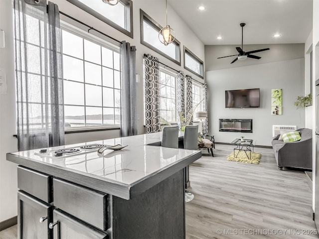 kitchen with a center island, hanging light fixtures, ceiling fan, light stone countertops, and light hardwood / wood-style floors