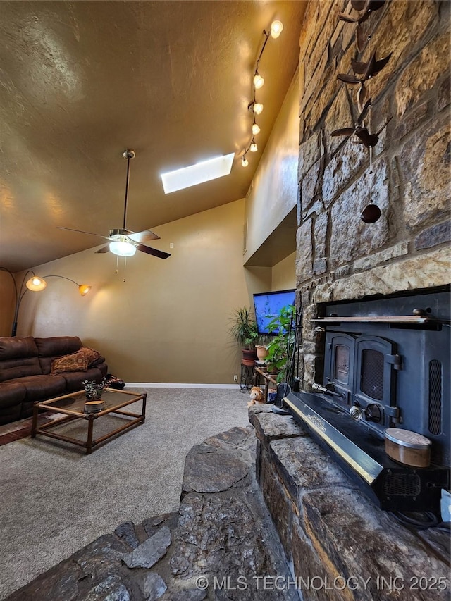 living room with ceiling fan, vaulted ceiling with skylight, carpet floors, a textured ceiling, and a wood stove