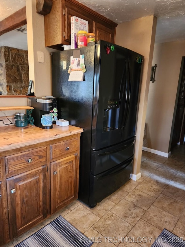 kitchen featuring butcher block countertops, light tile patterned floors, a textured ceiling, and black fridge with ice dispenser