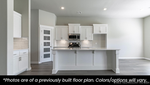 kitchen featuring white cabinets, a center island with sink, and tasteful backsplash