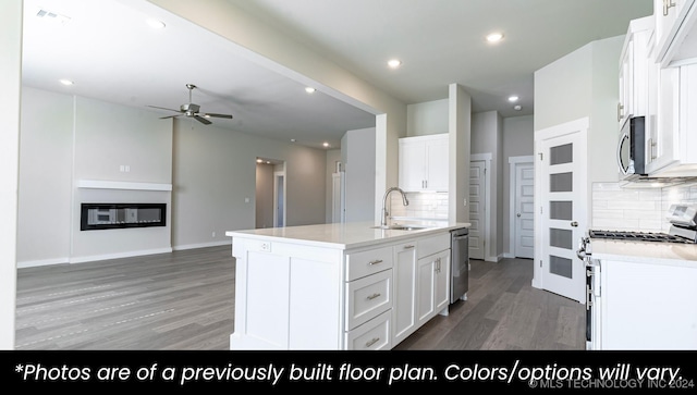 kitchen featuring white cabinetry, stainless steel appliances, decorative backsplash, a center island with sink, and hardwood / wood-style flooring