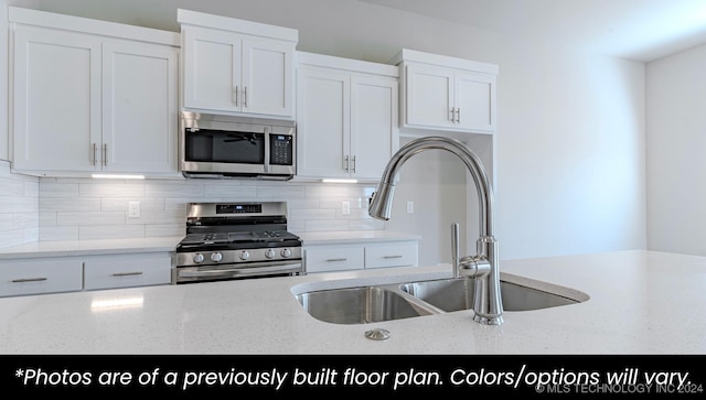 kitchen with white cabinets, sink, decorative backsplash, light stone counters, and stainless steel appliances