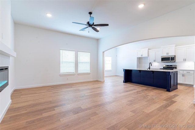 kitchen featuring light hardwood / wood-style flooring, an island with sink, white cabinets, stainless steel appliances, and backsplash