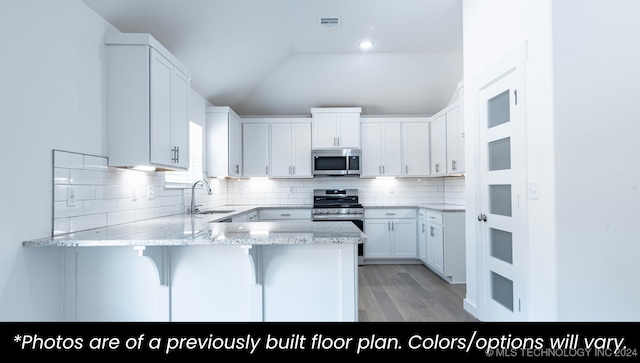 kitchen with sink, stainless steel appliances, kitchen peninsula, vaulted ceiling, and white cabinets