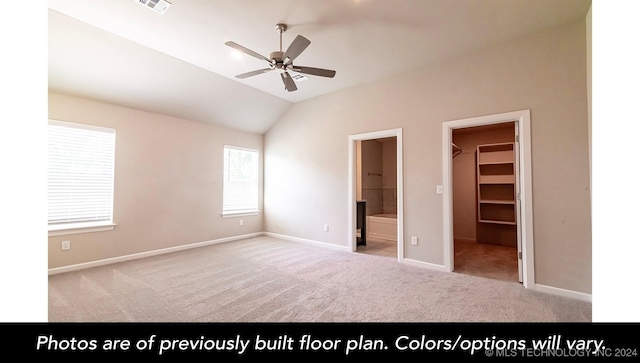 unfurnished bedroom with light carpet, a walk in closet, ensuite bath, vaulted ceiling, and ceiling fan