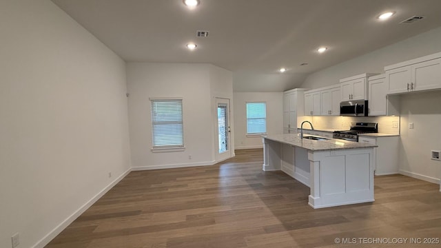 kitchen featuring white cabinetry, appliances with stainless steel finishes, an island with sink, light hardwood / wood-style floors, and decorative backsplash