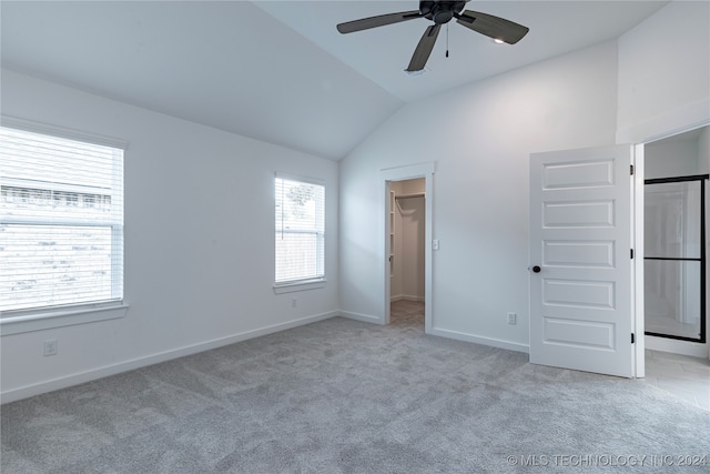 unfurnished bedroom with ceiling fan, light colored carpet, vaulted ceiling, a walk in closet, and a closet