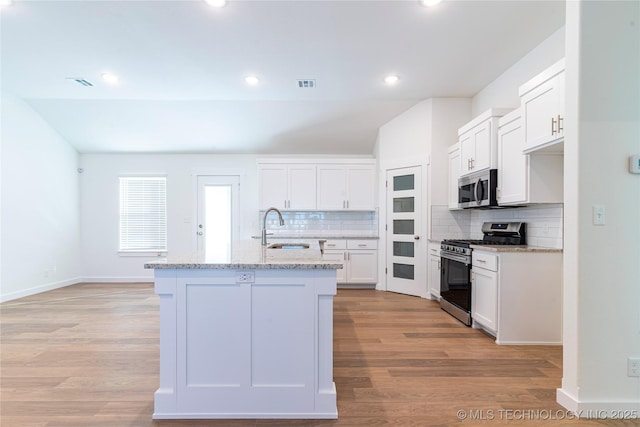 kitchen featuring light wood-type flooring, stainless steel appliances, sink, white cabinetry, and an island with sink