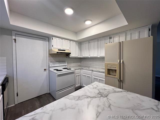 kitchen with white appliances, a tray ceiling, white cabinetry, and light stone counters