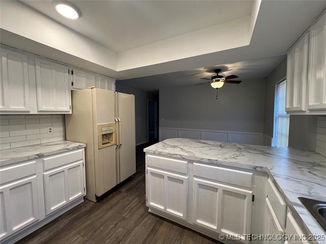 kitchen featuring white refrigerator with ice dispenser, backsplash, and white cabinetry