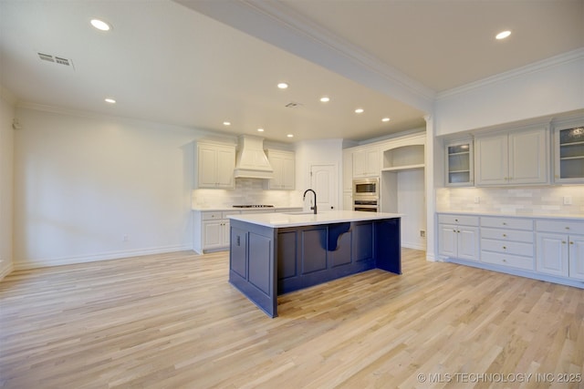 kitchen featuring ornamental molding, premium range hood, a kitchen island with sink, and stainless steel appliances