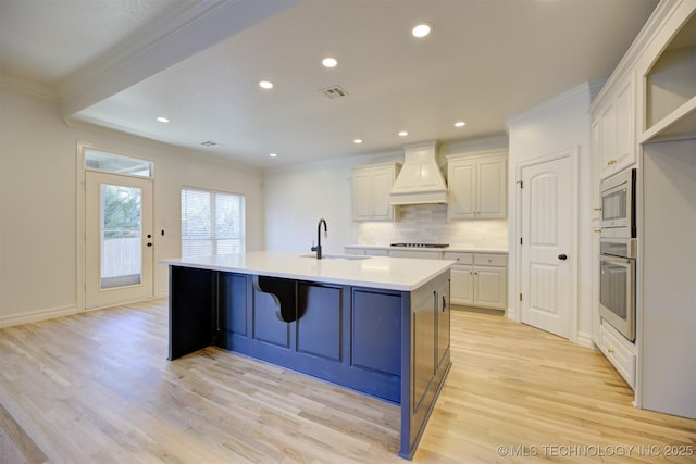 kitchen with premium range hood, a center island with sink, white cabinets, sink, and appliances with stainless steel finishes