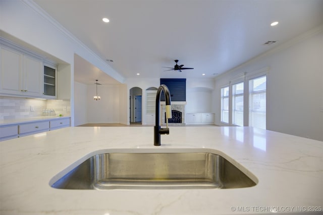 kitchen with tasteful backsplash, ceiling fan with notable chandelier, sink, decorative light fixtures, and a stone fireplace