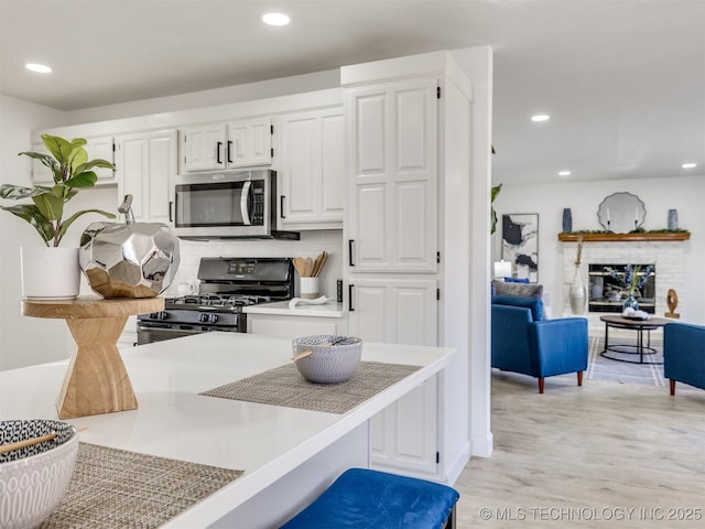 kitchen with white cabinets, black range with gas stovetop, light hardwood / wood-style flooring, and a brick fireplace