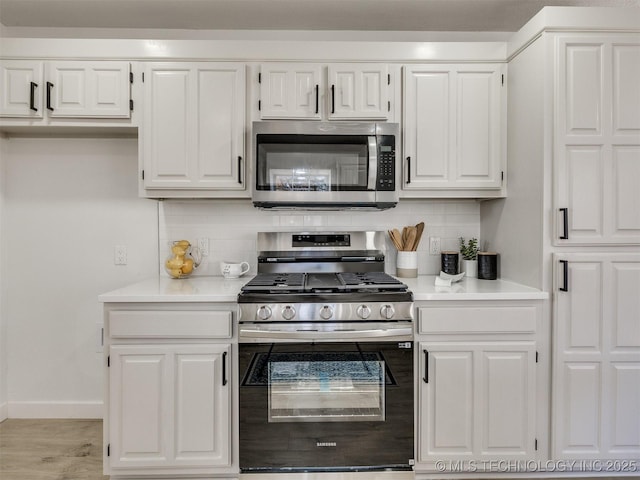 kitchen with white cabinets, backsplash, stainless steel appliances, and light hardwood / wood-style flooring