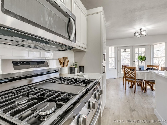 kitchen featuring french doors, white cabinets, appliances with stainless steel finishes, tasteful backsplash, and light hardwood / wood-style floors