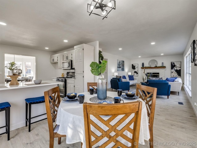 dining space with a chandelier, a brick fireplace, and light hardwood / wood-style flooring