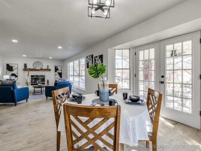 dining room featuring a fireplace, french doors, light hardwood / wood-style flooring, and ceiling fan