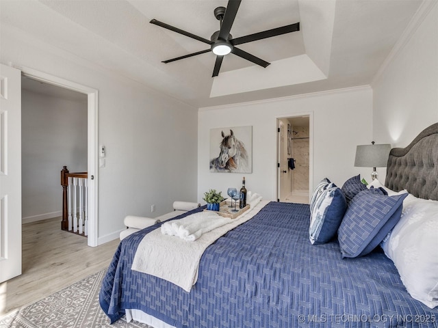 bedroom featuring a raised ceiling, crown molding, ceiling fan, light wood-type flooring, and connected bathroom