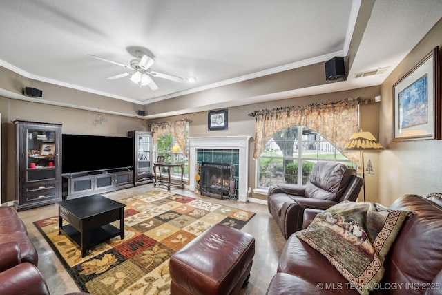 living room featuring ceiling fan, crown molding, and a tiled fireplace