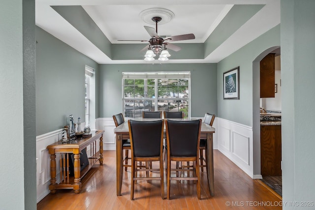 dining area featuring ceiling fan, wood-type flooring, ornamental molding, and a tray ceiling