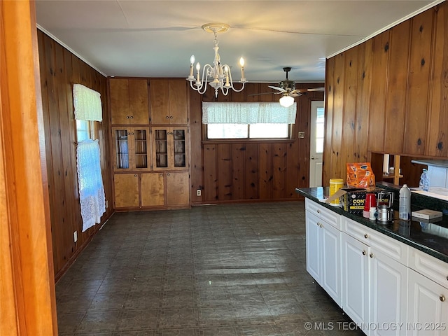 kitchen featuring white cabinets, ceiling fan with notable chandelier, and wooden walls