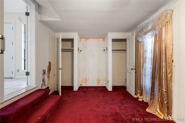 unfurnished bedroom with a textured ceiling, dark carpet, multiple closets, and wooden walls