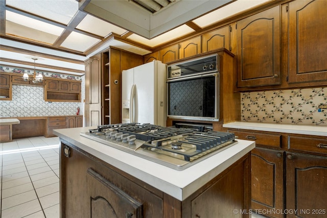 kitchen with an inviting chandelier, white refrigerator with ice dispenser, stainless steel gas stovetop, black oven, and light tile patterned floors