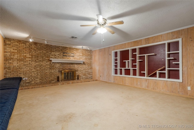 unfurnished living room with a textured ceiling, a brick fireplace, crown molding, and wood walls