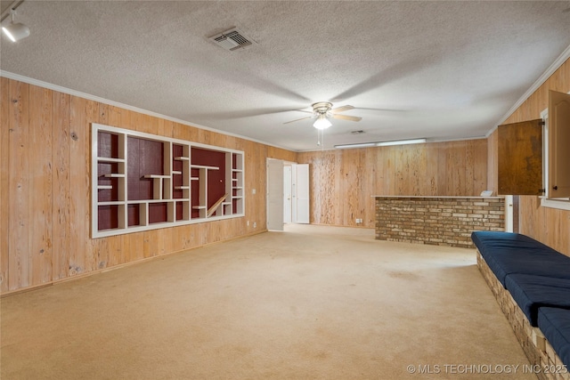 unfurnished living room featuring a textured ceiling, light colored carpet, ceiling fan, and ornamental molding