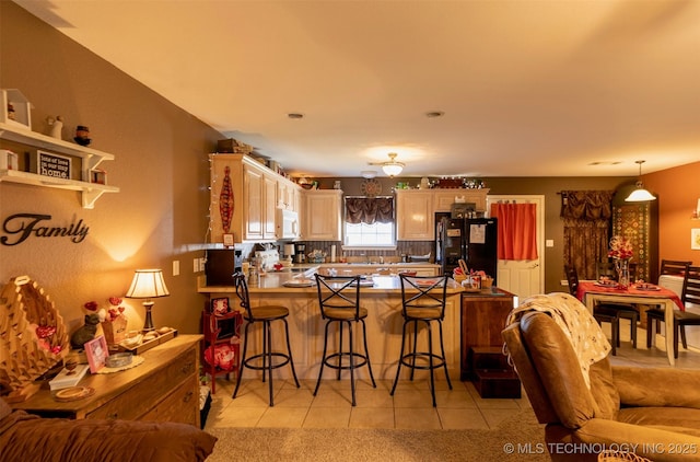 kitchen featuring a breakfast bar, kitchen peninsula, black refrigerator, light tile patterned flooring, and range