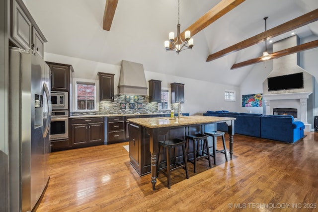 kitchen featuring a kitchen breakfast bar, a fireplace, appliances with stainless steel finishes, a center island with sink, and custom exhaust hood