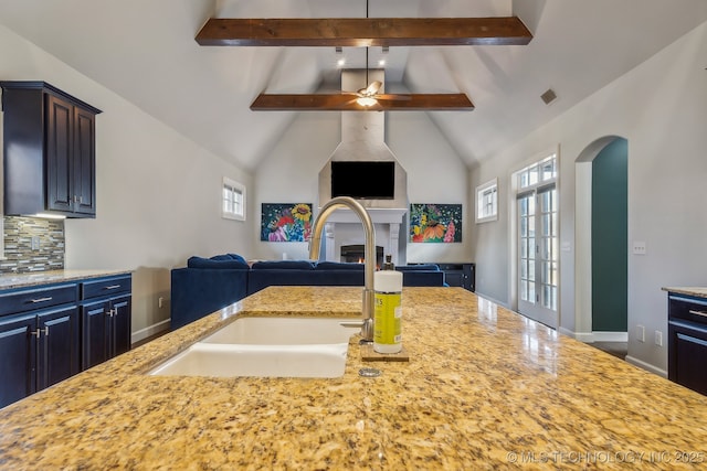 kitchen featuring sink, vaulted ceiling with beams, decorative backsplash, ceiling fan, and light stone counters