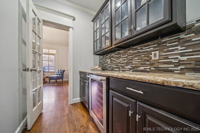 bar with dark wood-type flooring, beverage cooler, light stone counters, backsplash, and ornamental molding