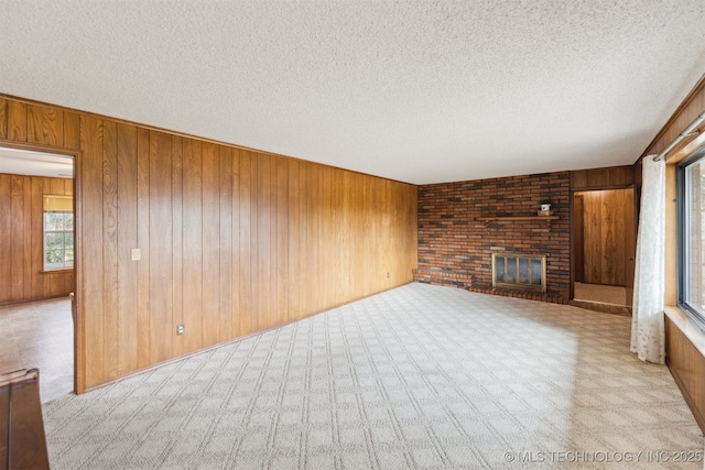 unfurnished living room featuring wood walls, a fireplace, light carpet, and a textured ceiling