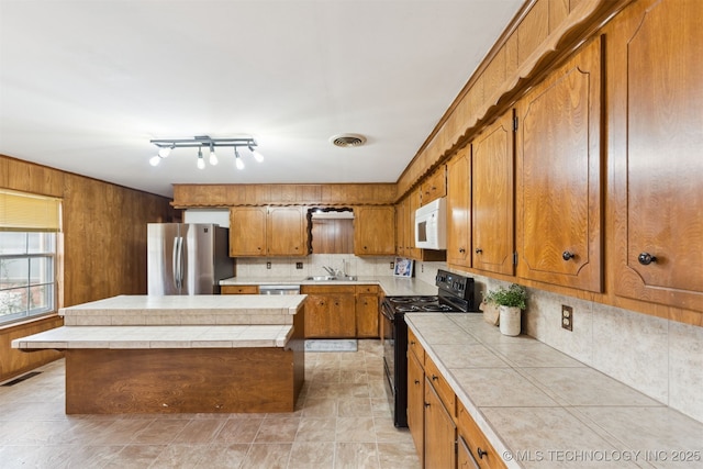 kitchen with a center island, tasteful backsplash, tile countertops, wood walls, and appliances with stainless steel finishes