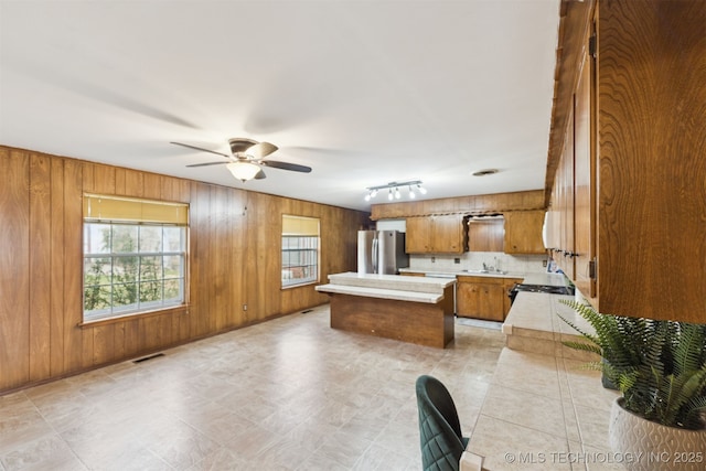 kitchen featuring stainless steel fridge, sink, ceiling fan, and wooden walls