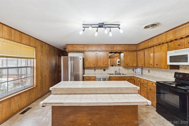 kitchen with wood walls, a center island, sink, tasteful backsplash, and stainless steel appliances