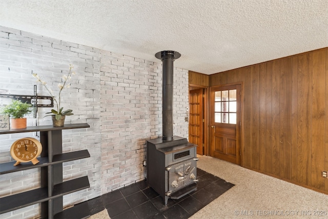 carpeted living room featuring a wood stove, wood walls, brick wall, and a textured ceiling