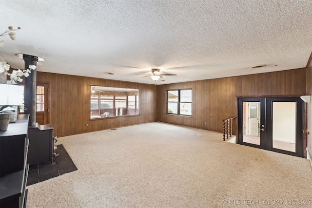 unfurnished living room featuring a wood stove, ceiling fan, dark carpet, and a textured ceiling