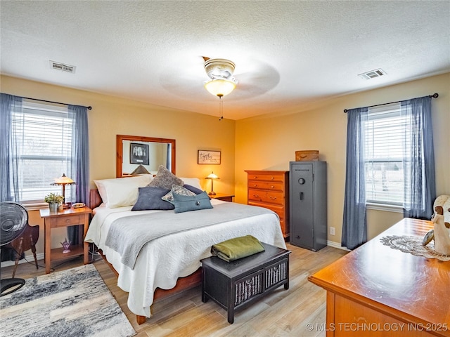 bedroom with multiple windows, light wood-type flooring, a textured ceiling, and ceiling fan