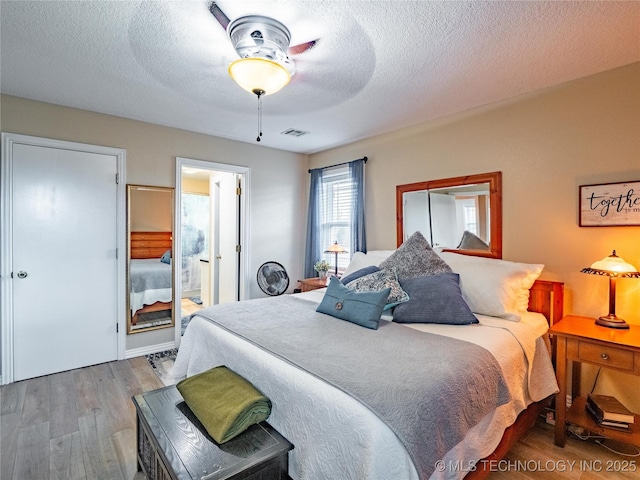 bedroom featuring hardwood / wood-style floors, a textured ceiling, ceiling fan, and ensuite bath