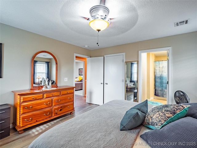 bedroom with wood-type flooring, connected bathroom, a textured ceiling, and ceiling fan