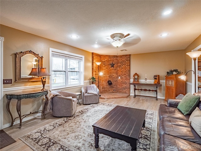 living room with ceiling fan, a brick fireplace, hardwood / wood-style floors, and a textured ceiling