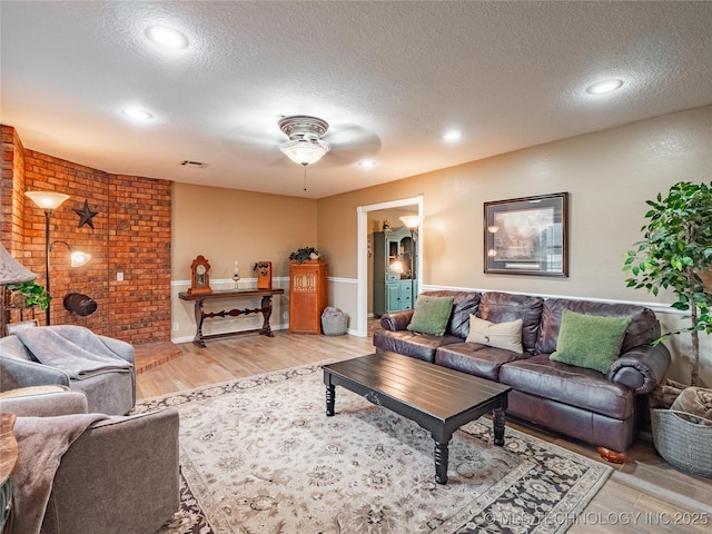 living room featuring ceiling fan, a textured ceiling, and light hardwood / wood-style flooring