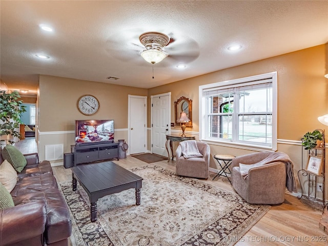 living room featuring ceiling fan, light hardwood / wood-style flooring, and a textured ceiling