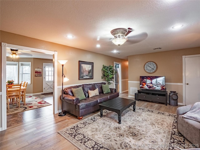 living room featuring ceiling fan, light hardwood / wood-style flooring, and a textured ceiling