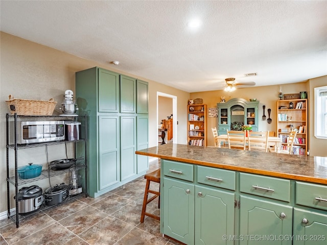 kitchen featuring ceiling fan, a kitchen breakfast bar, green cabinets, and a textured ceiling