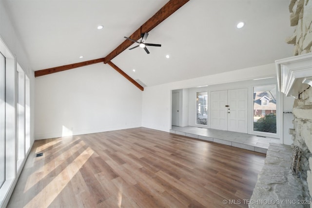 unfurnished living room featuring beam ceiling, a stone fireplace, ceiling fan, and wood-type flooring